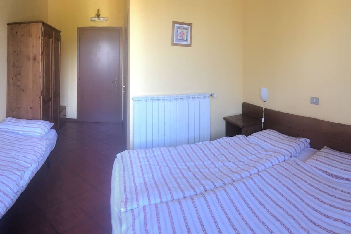 Ein Zimmer mit zwei Betten, einem Holzschrank, einem Schreibtisch mit Telefon und Fernseher sowie einem Heizkörper.