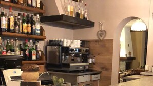 Una zona de bar con una máquina de café, estantes llenos de botellas de licores y una decoración con forma de corazón en la pared.