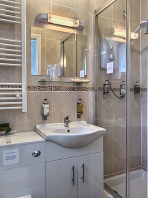 A bathroom with a glass shower enclosure, a white sink with a mirror above it, and a towel rack. - Grove House (Leyburn)