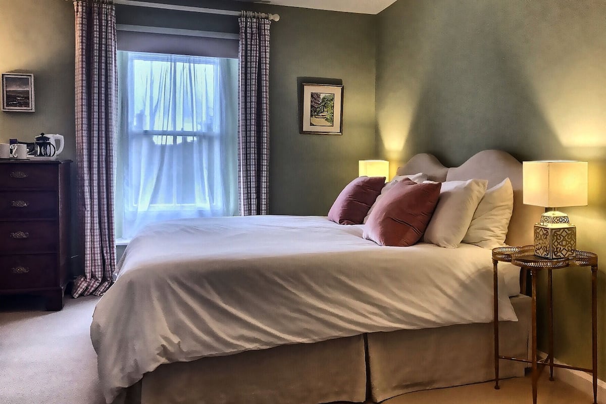 A bedroom with a bed, a nightstand, a dresser, and a window with curtains.
