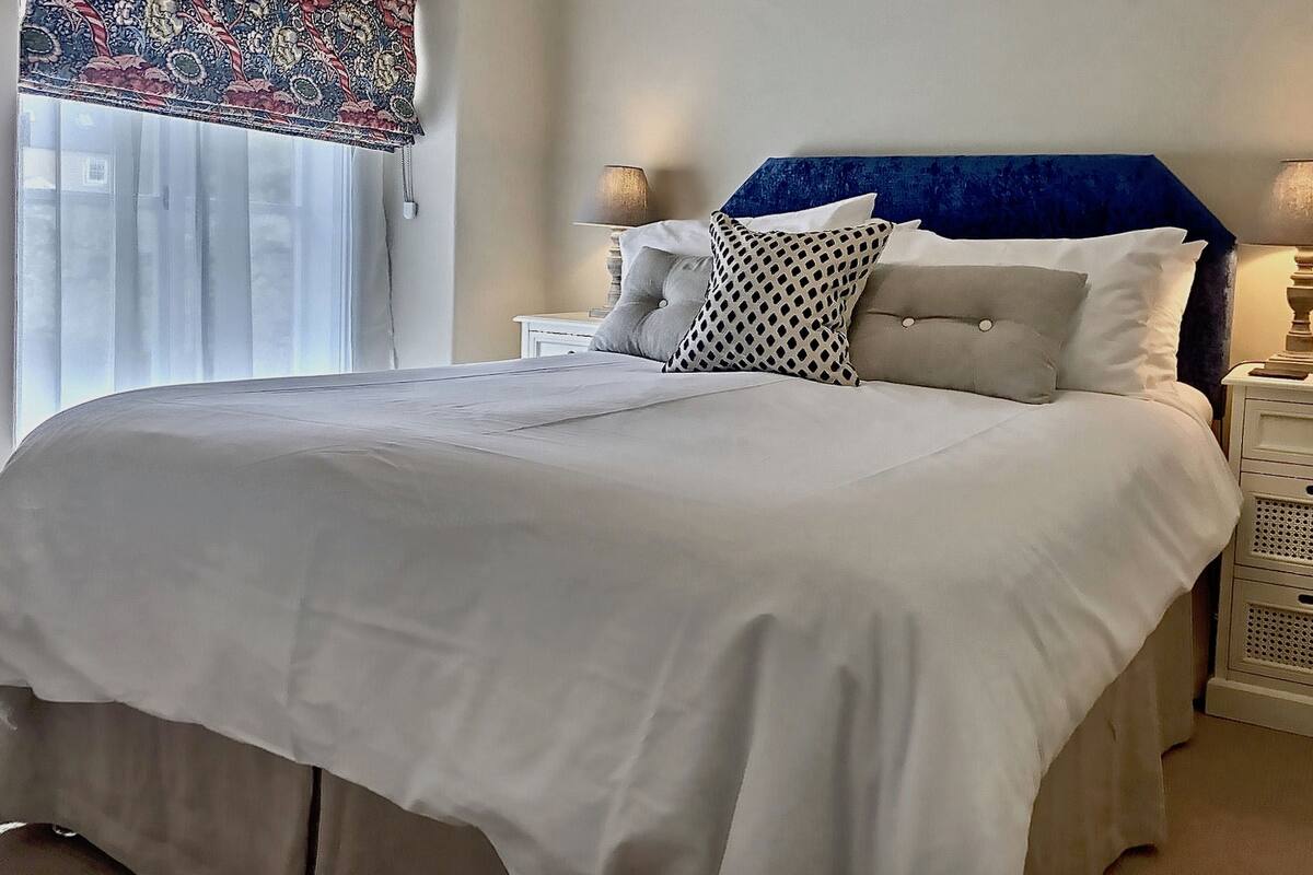 A neatly made bed with white bedding, a blue headboard, and two bedside tables with lamps.