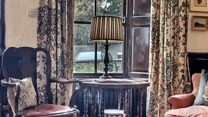 A traditional room with a wooden chair, a table with a glass top, and a window with curtains. - Grove House (Leyburn)
