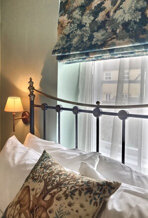 A bed with white linens, a floral-patterned pillow, and a metal headboard. - Grove House (Leyburn)
