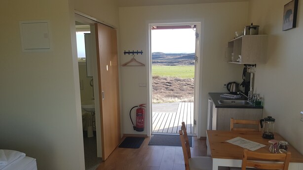Una habitación con cama, una mesa de comedor con sillas, una zona de cocina con fregadero y un extintor.