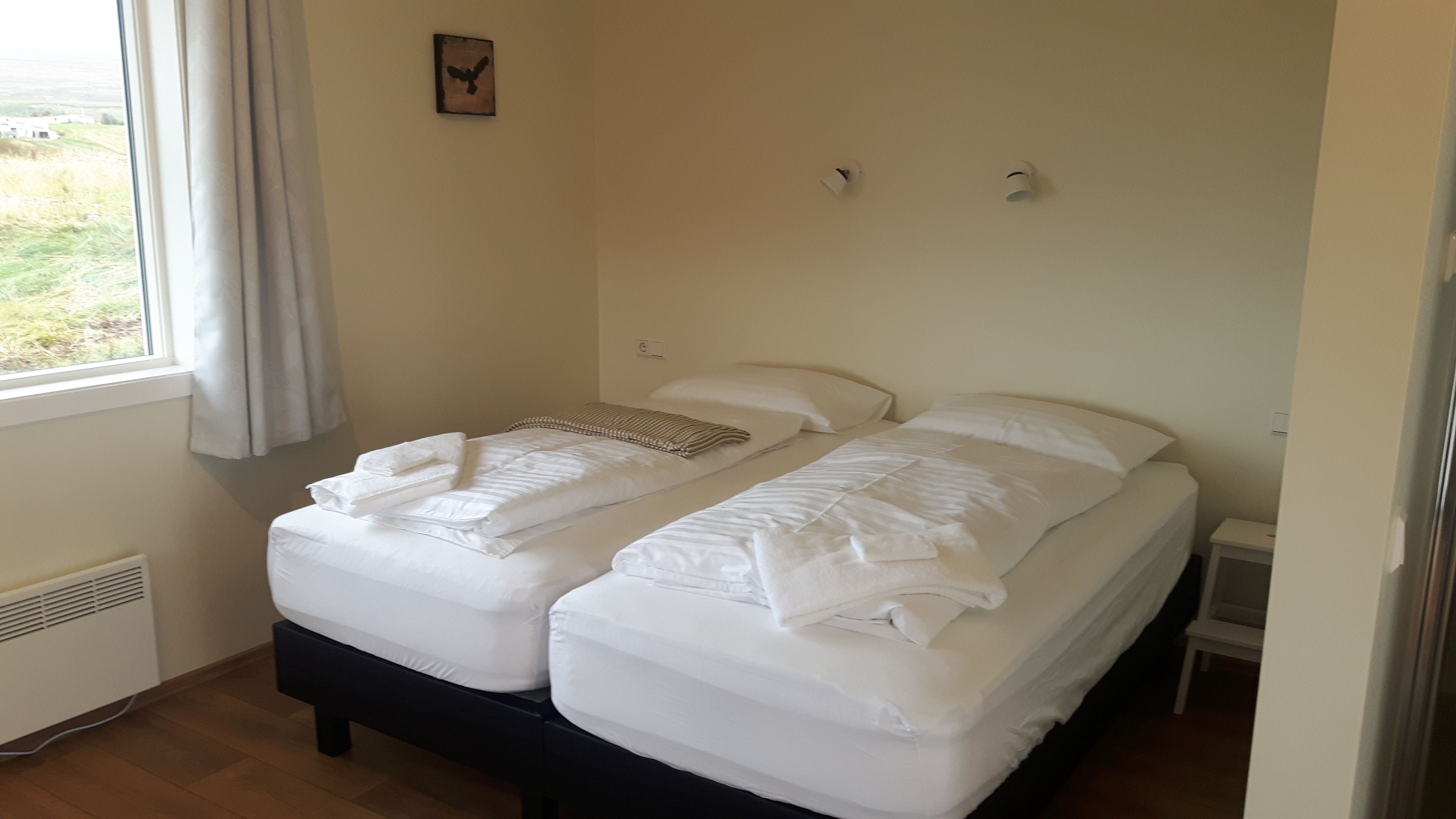 Una cama doble con ropa de cama blanca, una mesita de noche, un calentador y una ventana con cortinas.