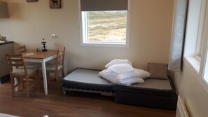 A small room with a bed, a desk, and a chair. There is a window with a view of a grassy field.