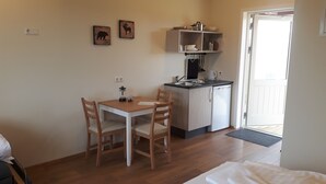 Una pequeña cocina americana con un lavamanos, una cafetera y un microondas. Hay una mesa de comedor con dos sillas y una alfombra pequeña cerca de la puerta.