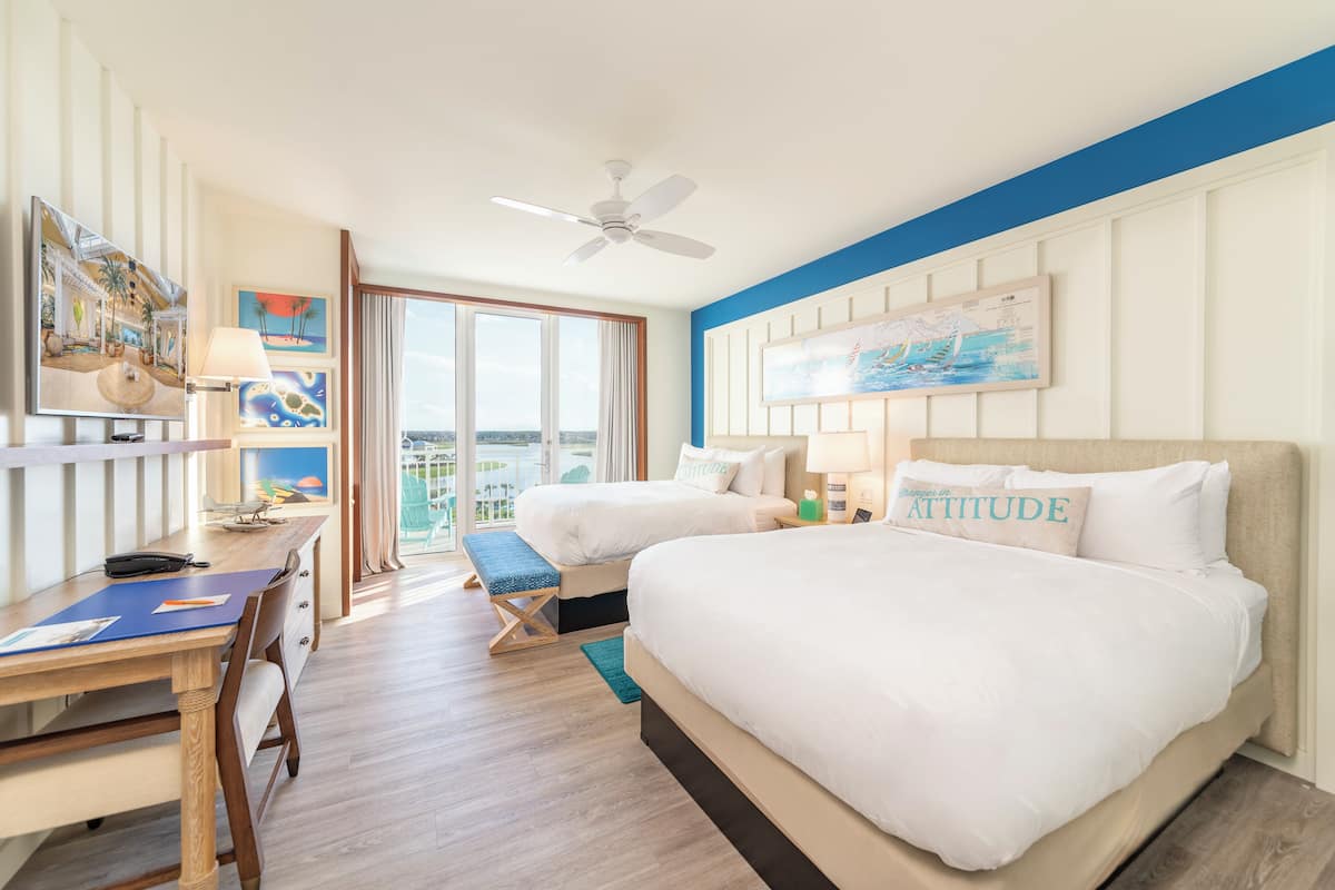 Ein Hotelzimmer mit zwei Betten, einem Schreibtisch mit Stuhl, einem Deckenventilator und Bildern an den Wänden.