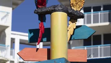 Ein Wegweiser mit bunten Papageien darauf, der zu Annehmlichkeiten wie 'Guest Towels' und 'Sally Rim Bar & Grill' weist.