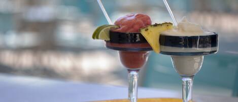 Two cocktails in martini glasses with garnishes, placed on a table with a tropical-themed coaster.