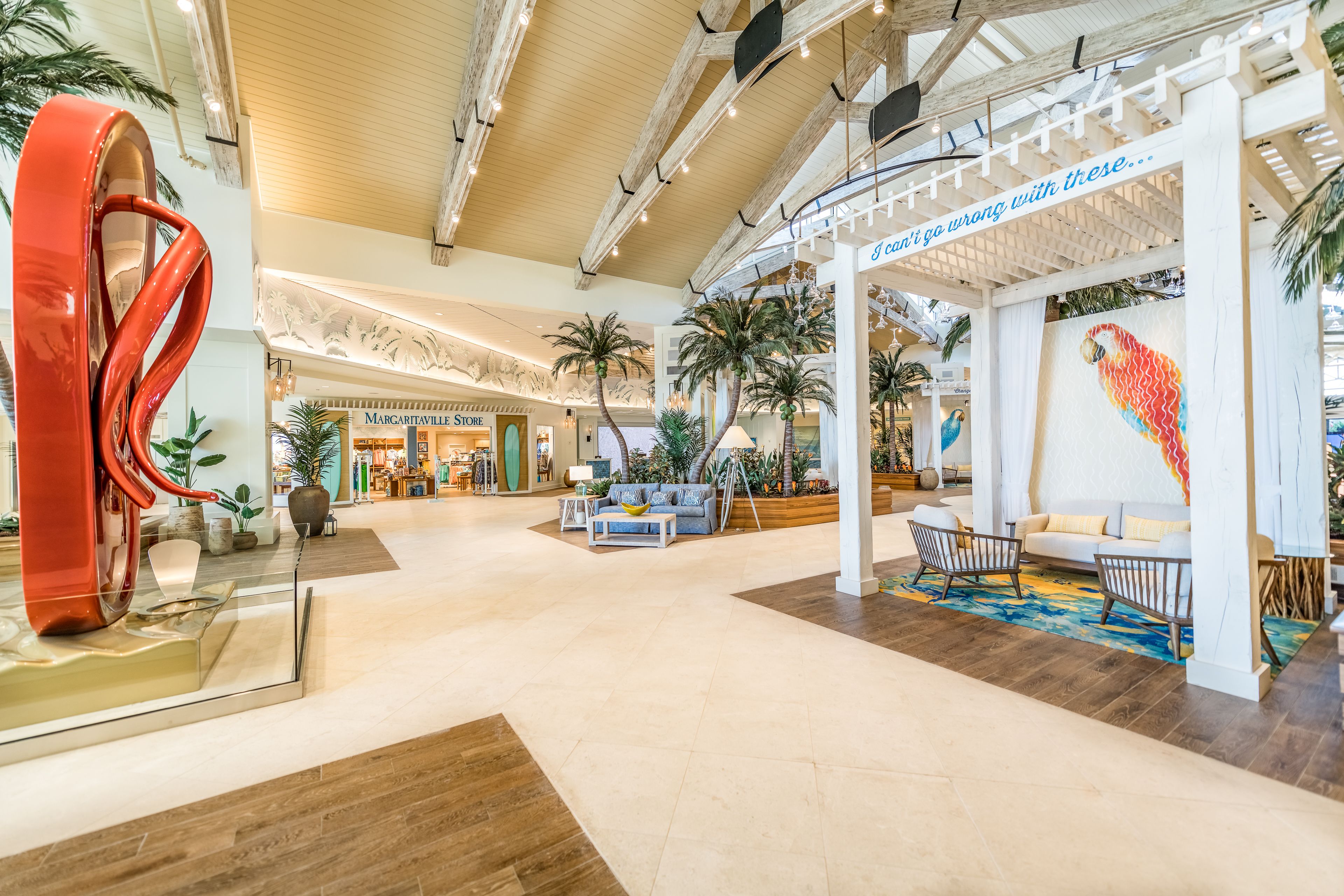 A spacious lobby with a modern design, featuring a large abstract sculpture, a seating area with sofas and chairs, and a decorative wall with a colorful bird mural.