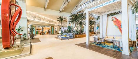 A spacious lobby with a modern design, featuring a large abstract sculpture, a seating area with sofas and chairs, and a decorative wall with a colorful bird mural.