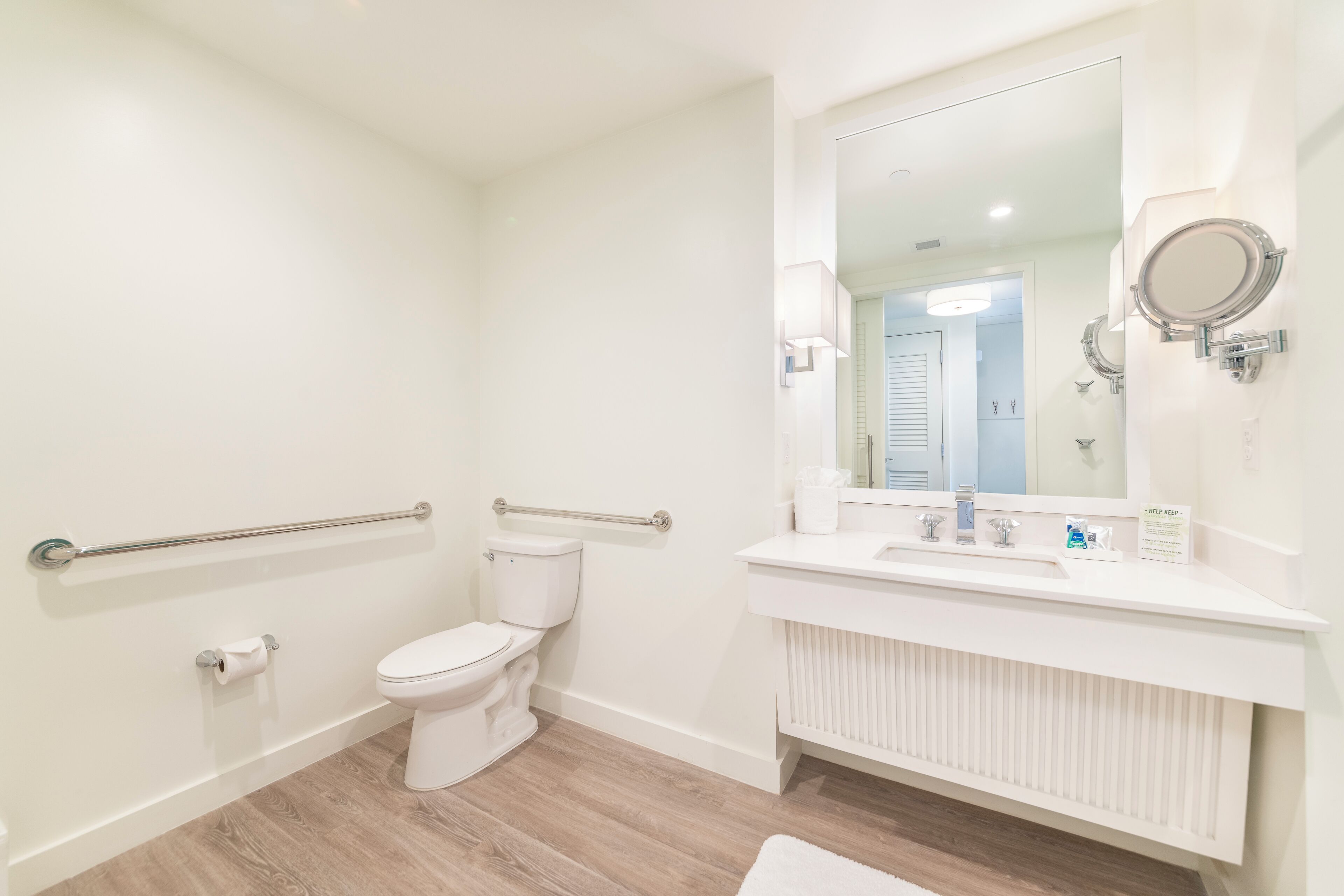 Een moderne badkamer met toilet, wastafel met spiegel en een handgreep.