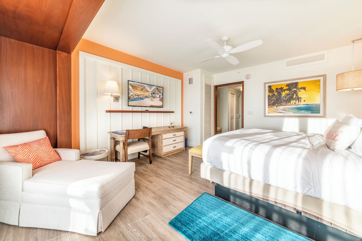 Ein Hotelzimmer mit Bett, Schreibtisch, Sessel, Sofa und Fernseher.