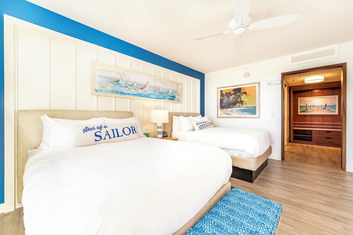 Ein Hotelzimmer mit zwei Betten, einem Deckenventilator und Bildern an den Wänden.