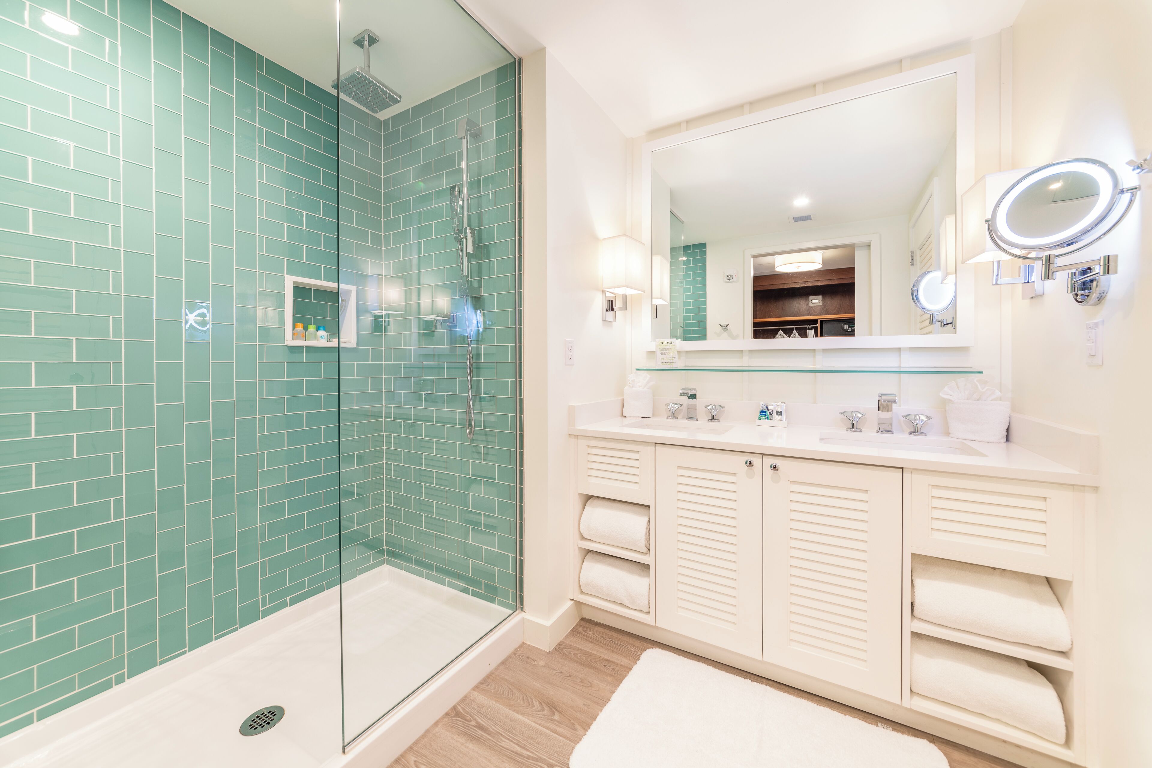 A bathroom with a glass-enclosed shower, a large mirror with lights, and a vanity with a sink and towel racks.