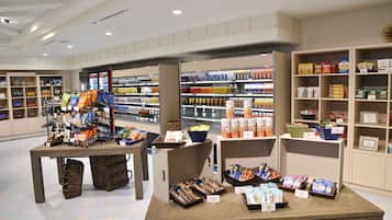 Un magasin bien organisé, avec des étagères remplies de divers produits, une table de présentation où sont exposées des collations, et un intérieur propre et moderne.