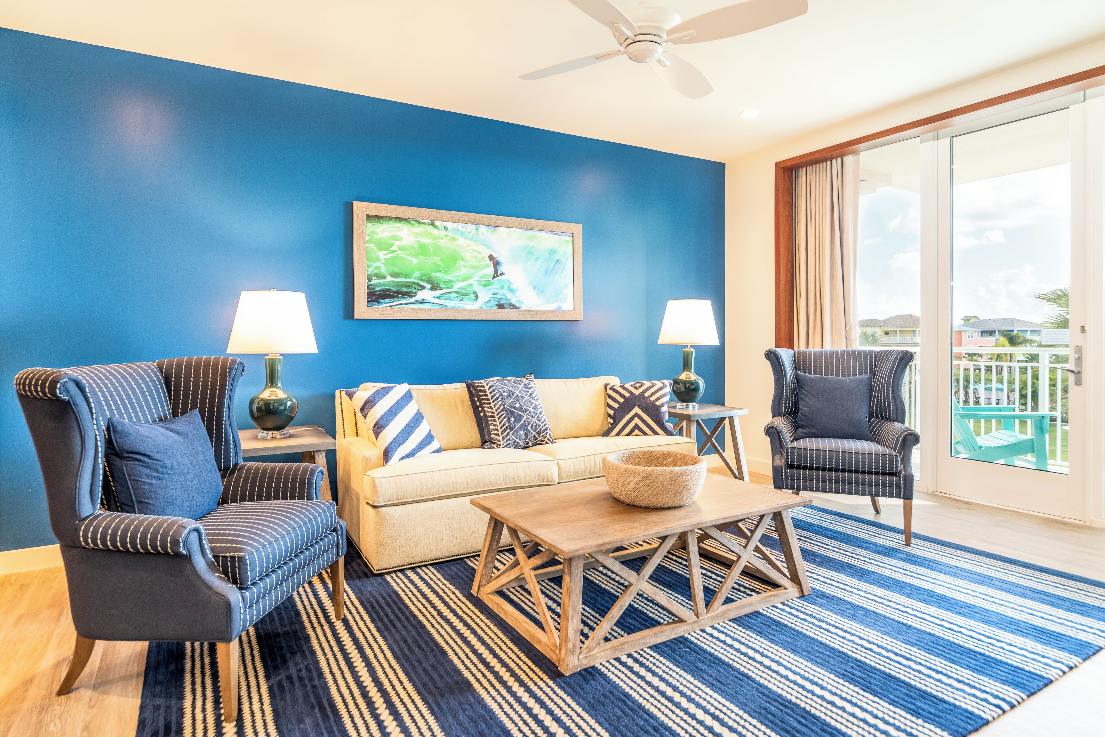 A living room with a blue wall, a sofa, two armchairs, a coffee table, and a ceiling fan.