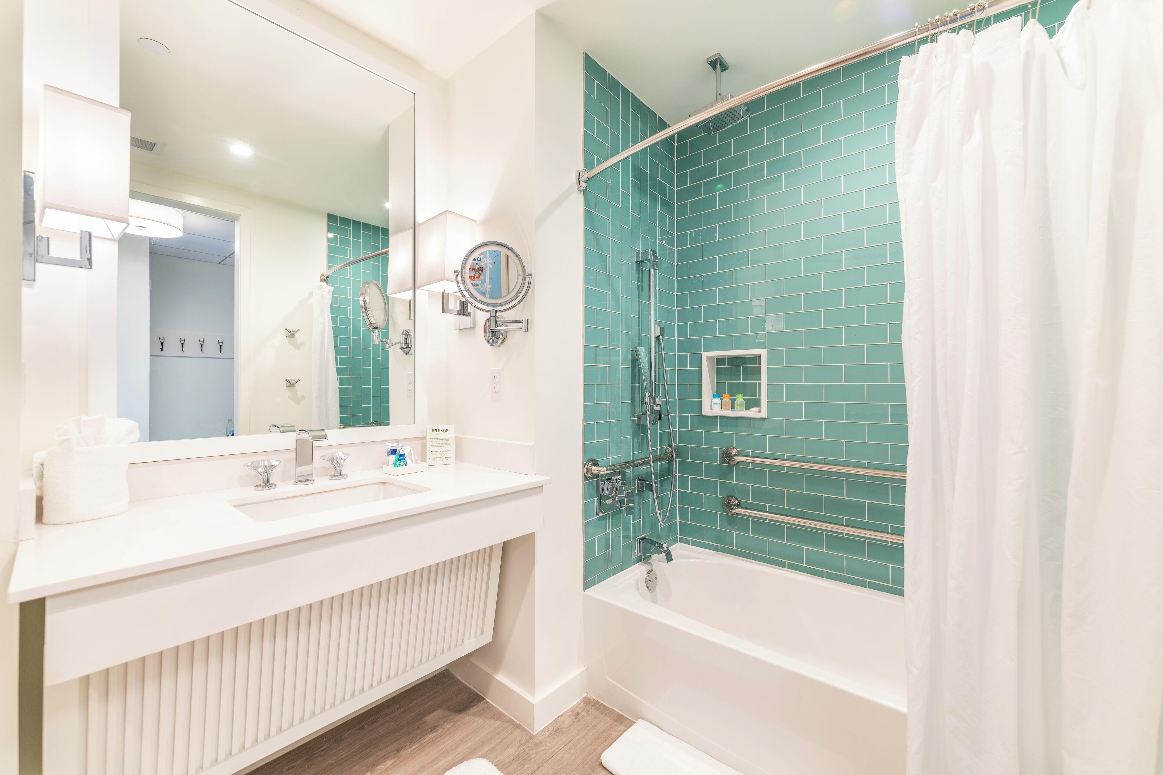 A modern bathroom with a white vanity, a large mirror, a bathtub, and a shower area with teal tiles.