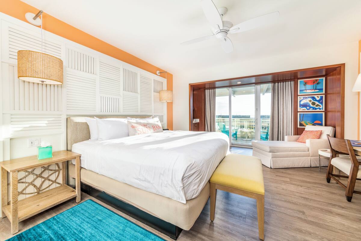 Ein Hotelzimmer mit einem großen Bett, einem Nachttisch aus Holz, einer Bank, einem Essbereich und Blick ins Freie.