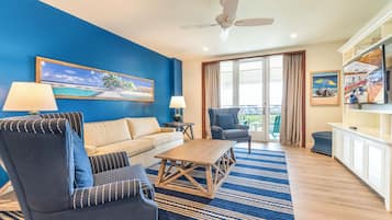 Een woonkamer met een blauwe wand, een bank, twee fauteuils, een salontafel, een plafondventilator en uitzicht op de omgeving.