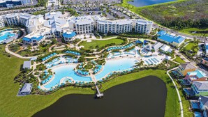 An aerial view of a resort with multiple swimming pools, a large central pool, and surrounding greenery.