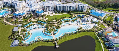 Vista aérea de um resort com várias piscinas, incluindo uma grande piscina central, e vegetação ao redor.