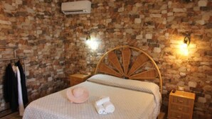 A bedroom with a stone wall, a wooden ceiling, a bed with a woven headboard, a bedside table, and a basket.