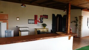 A kitchen with a wooden countertop, a water dispenser, a refrigerator, and a table with chairs. There are wall-mounted lights and a potted plant on the wall.