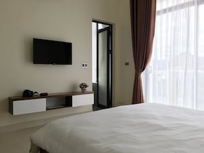 Habitación de hotel con cama, televisor de pantalla plana montado en la pared, mesita de noche con una planta y puerta corrediza al exterior.