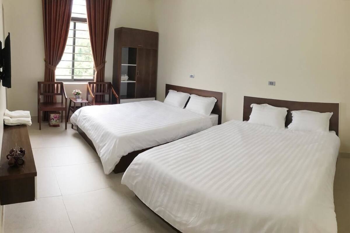 A hotel room with two beds, a desk, a chair, a wardrobe, and a TV.