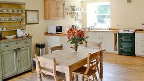 A kitchen with a wooden table, chairs, a microwave, and a green appliance. - Finzean Estate Holiday Cottages (Banchory)