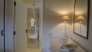 A bathroom with a towel rack, a mirror, and a bedside table with a book and a lamp. - Finzean Estate Holiday Cottages (Banchory)