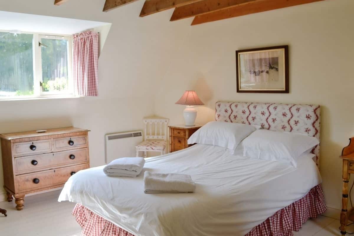 A bedroom with a bed, a dresser, a chair, a nightstand with a lamp, and a window with curtains.