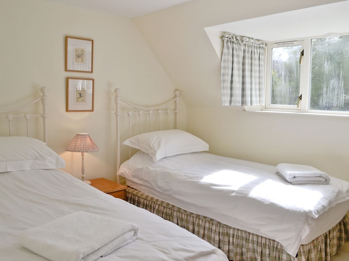 A bedroom with two single beds, a nightstand with a lamp, and a window with curtains.