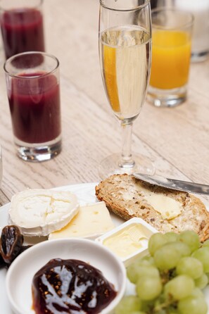 Een tafel met een schaal kaas, crackers en druiven, vergezeld van glazen sap en een fles champagne.