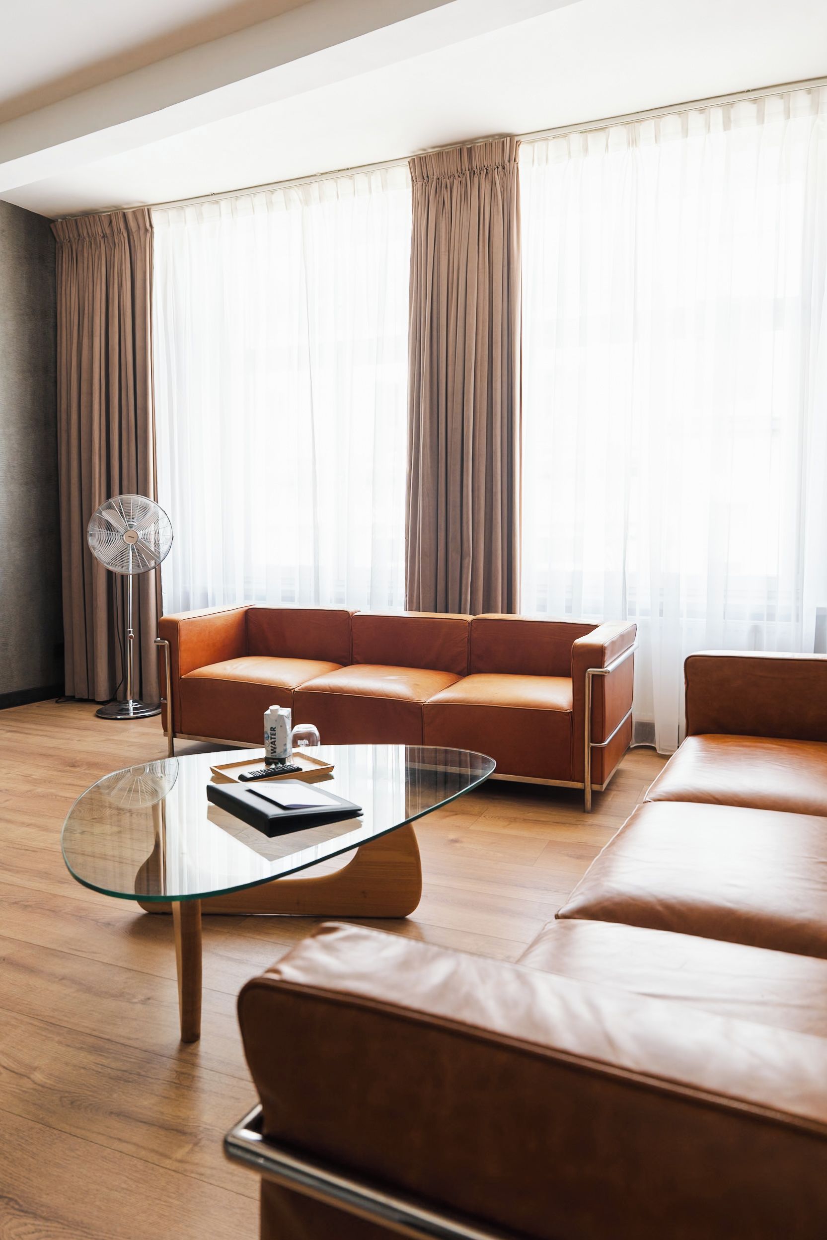 Una sala de estar moderna con un sofá de cuero, una mesa de centro de vidrio y un ventilador de pie.