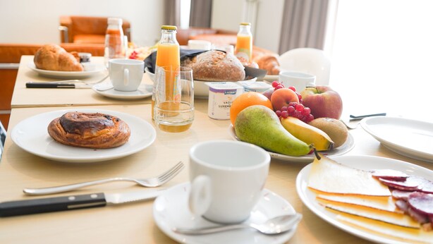 Una mesa de desayuno con cruasanes, pan, frutas y bebidas.