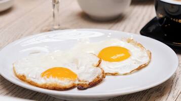A breakfast setting with two fried eggs on a plate, a glass of orange juice, and a coffee maker on the table.