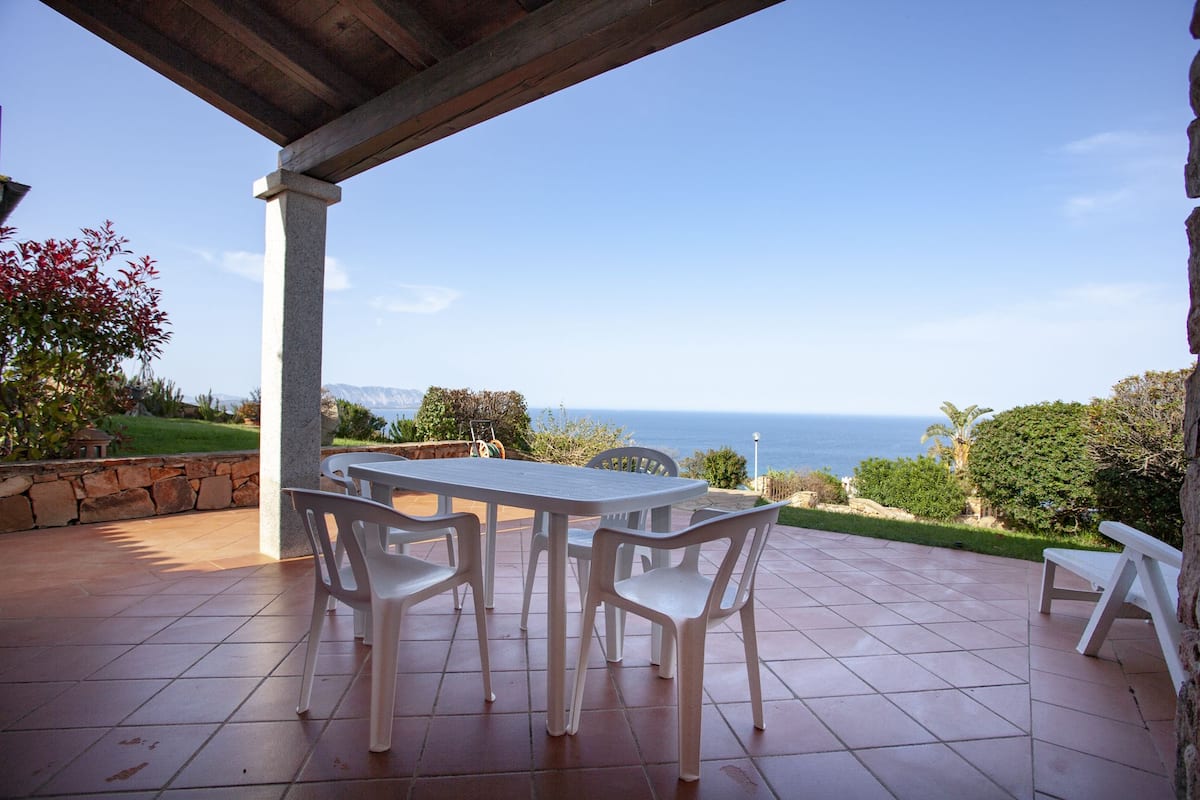 Un patio exterior con una mesa y sillas, un muro de piedra y vistas al mar.
