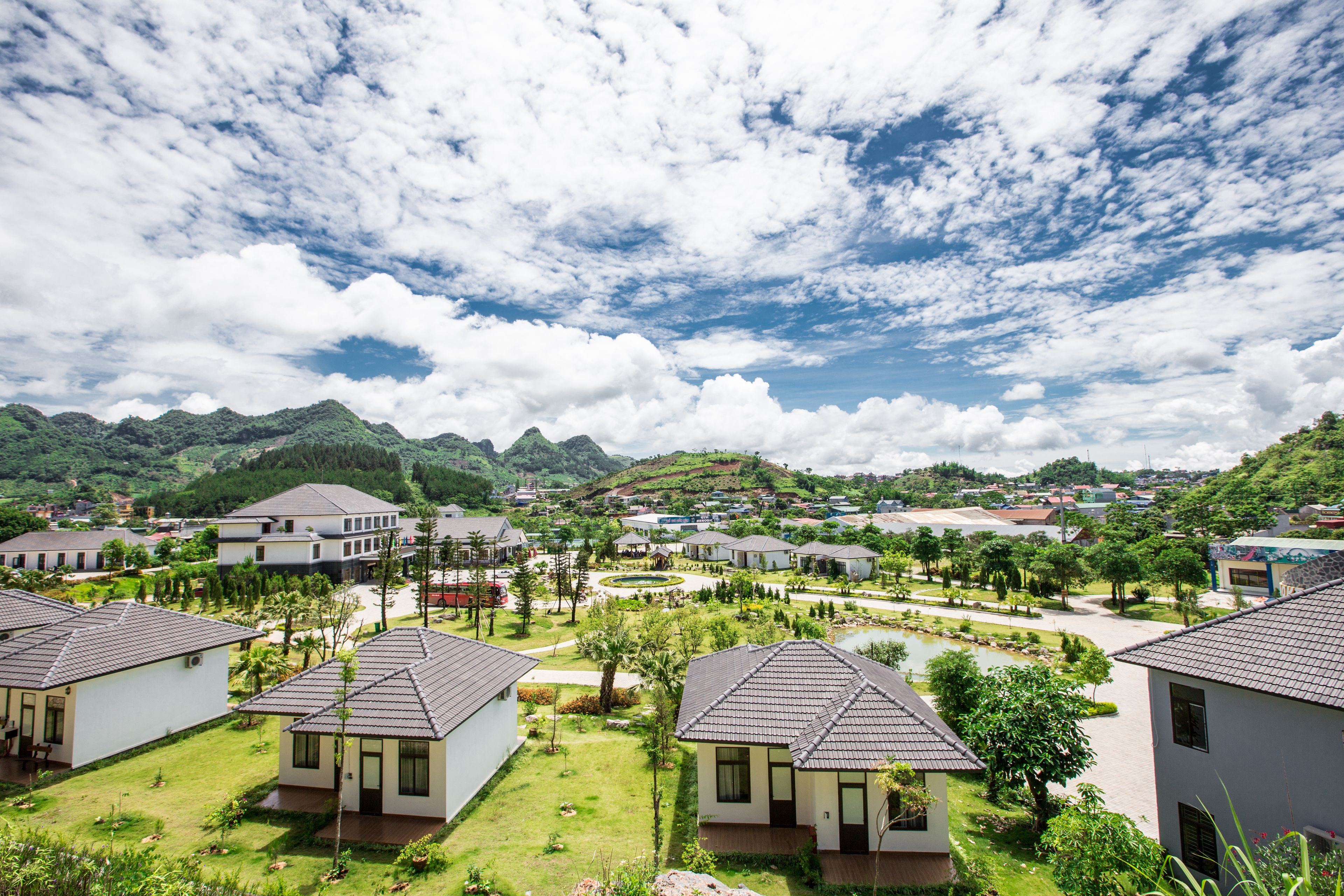 A residential area with houses, a small pond, and a hilly landscape in the background.