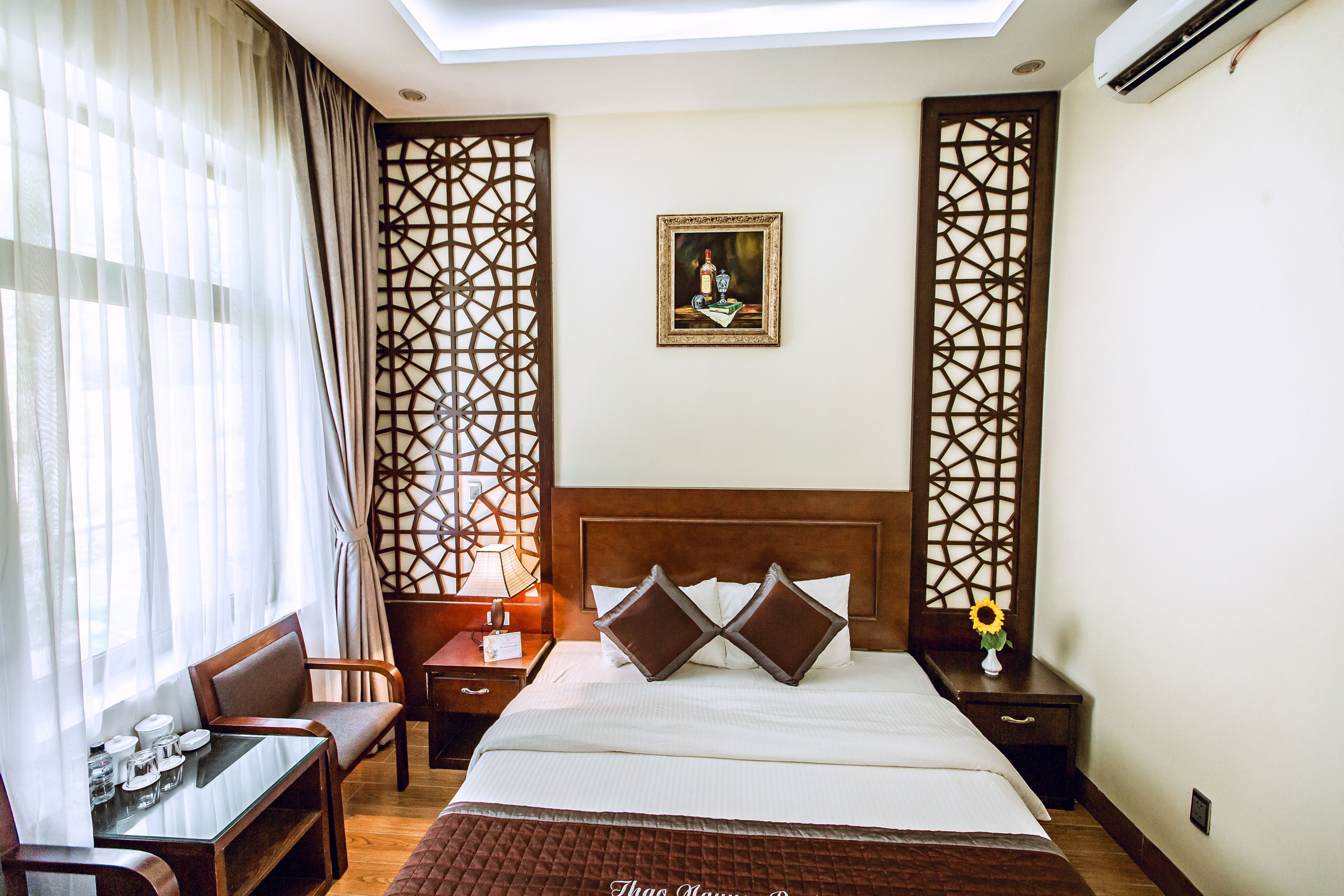 A hotel room with a bed, a desk, a chair, a nightstand, and a decorative wall panel.