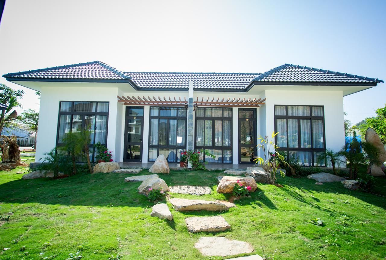 A modern two-story house with a tiled roof, large windows, and a well-maintained garden with rocks and plants.