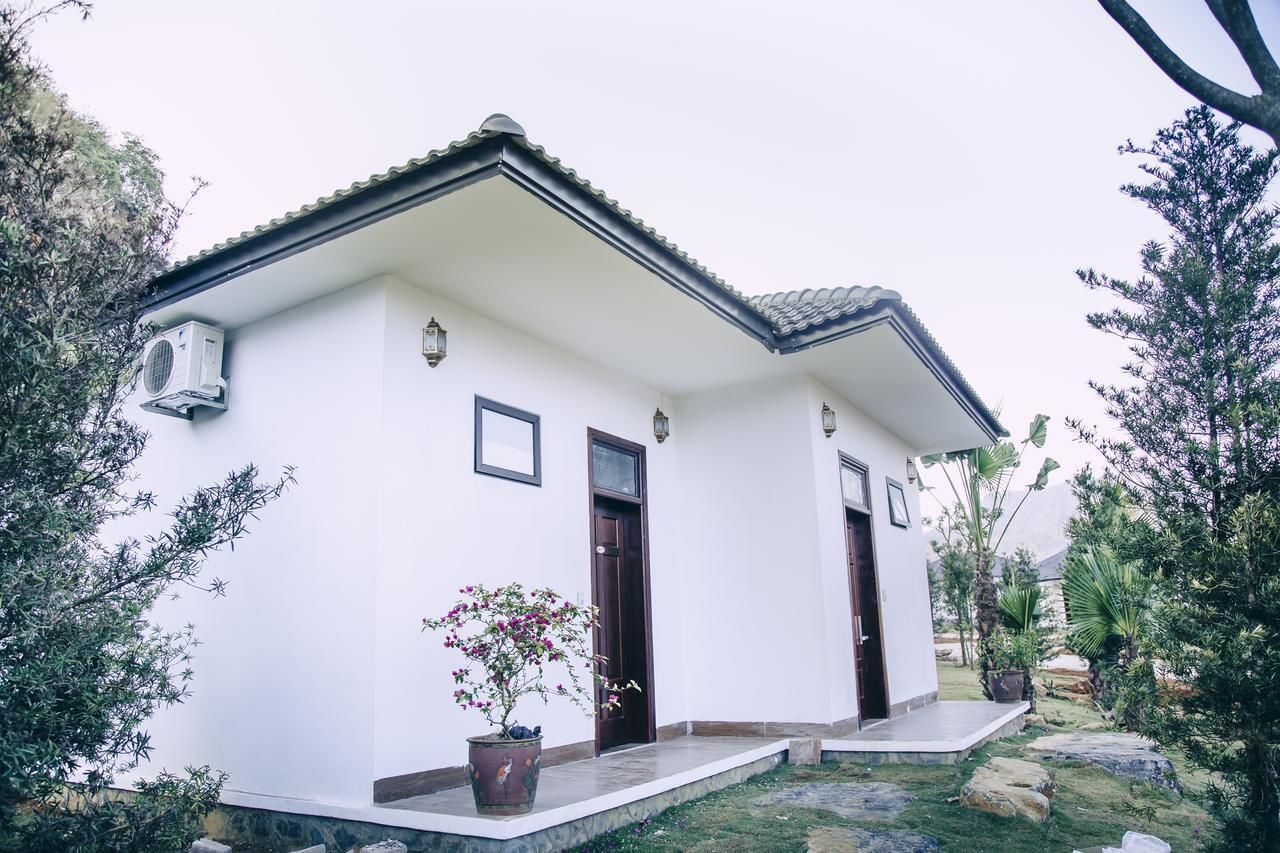 A white building with a tiled roof, two doors, and a small porch with potted plants.
