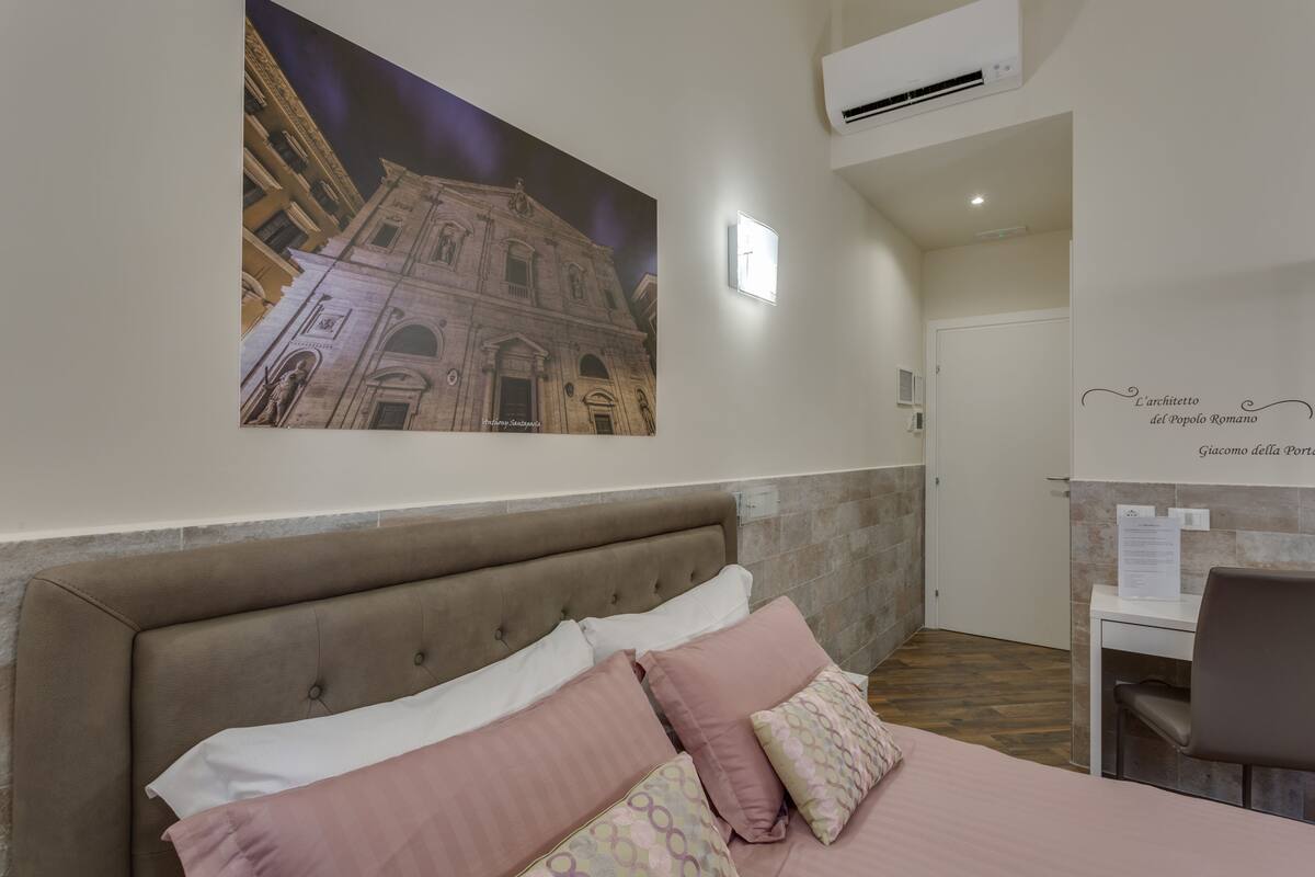 A hotel room with a large bed, a desk, and a wall-mounted air conditioner.