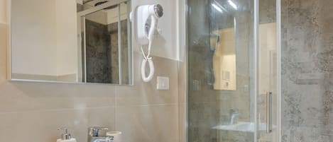 Ein modernes Badezimmer mit einem weißen Waschbecken, einer Duschkabine aus Glas und einem großen Spiegel.