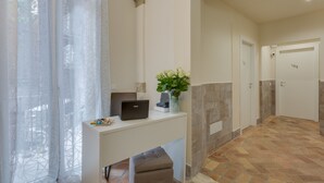 Zona de recepción de un hotel con un escritorio, una computadora portátil, un jarrón con flores y una puerta con el número 105.