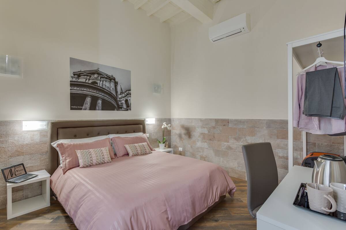 A bedroom with a bed, a nightstand, a desk, a chair, and a wall-mounted air conditioner.