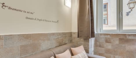 A room with a beige sofa, a wall-mounted clock, and a window with a curtain.