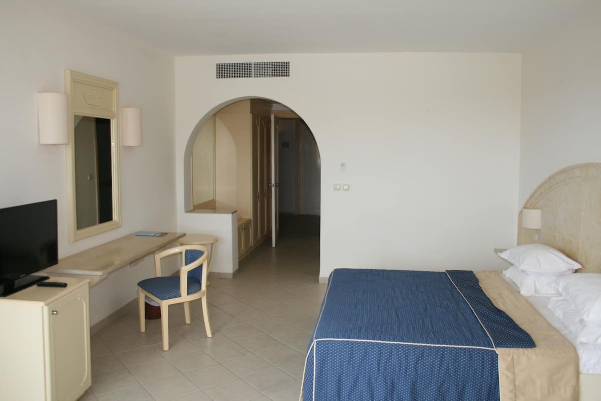 A hotel room with a bed, a desk with a chair, a television, and a bathroom visible through an archway.